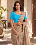 Aqua blue front-hook saree blouse worn with a beige linen saree, standing in a sunlit courtyard doorway
