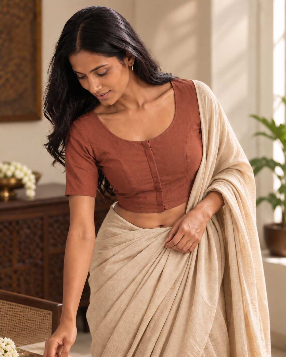 Terracotta front-hook saree blouse worn with a beige linen saree, adjusting the pallu indoors