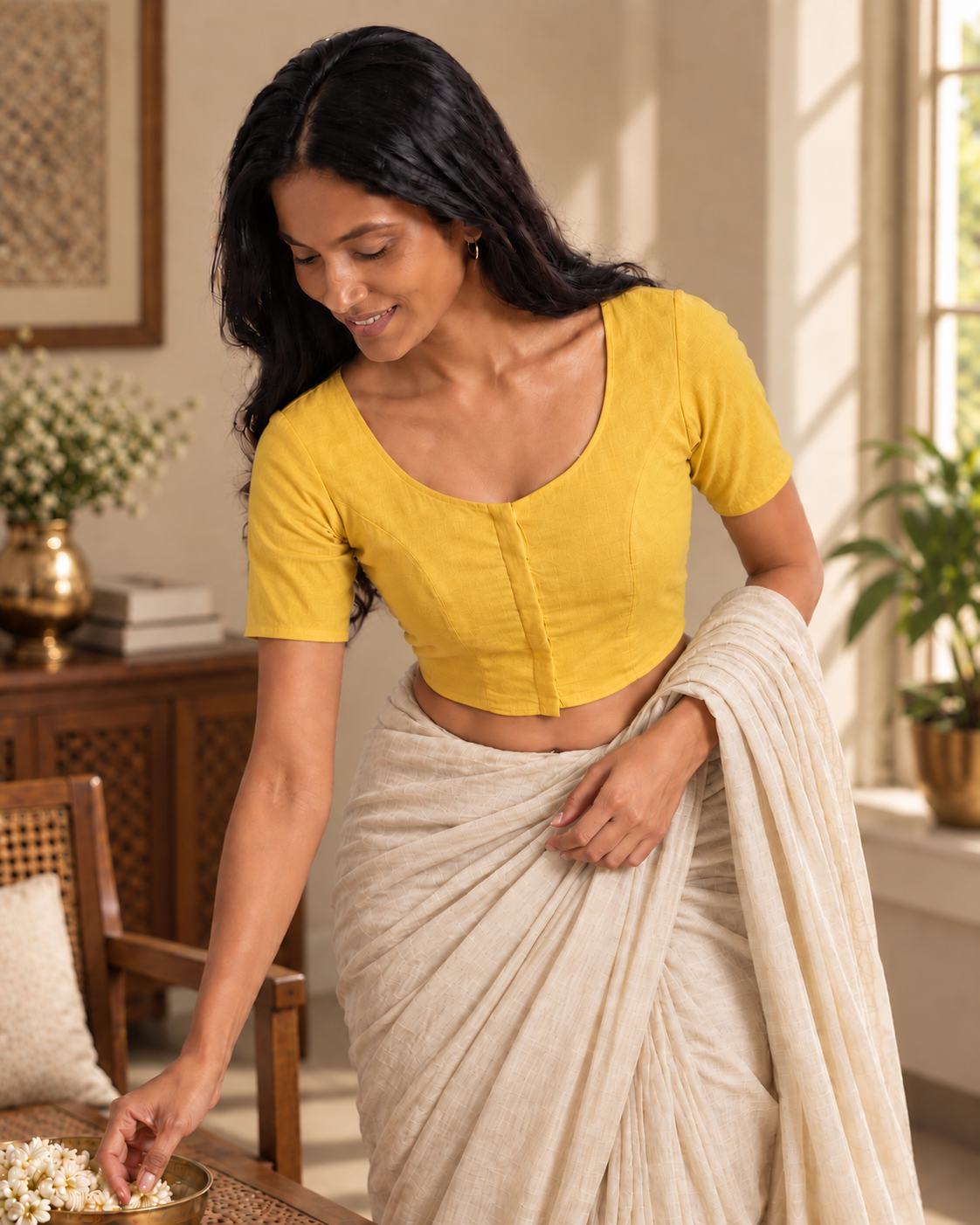 Sunshine yellow front-hook saree blouse worn with a beige saree, bending to arrange flowers on a table