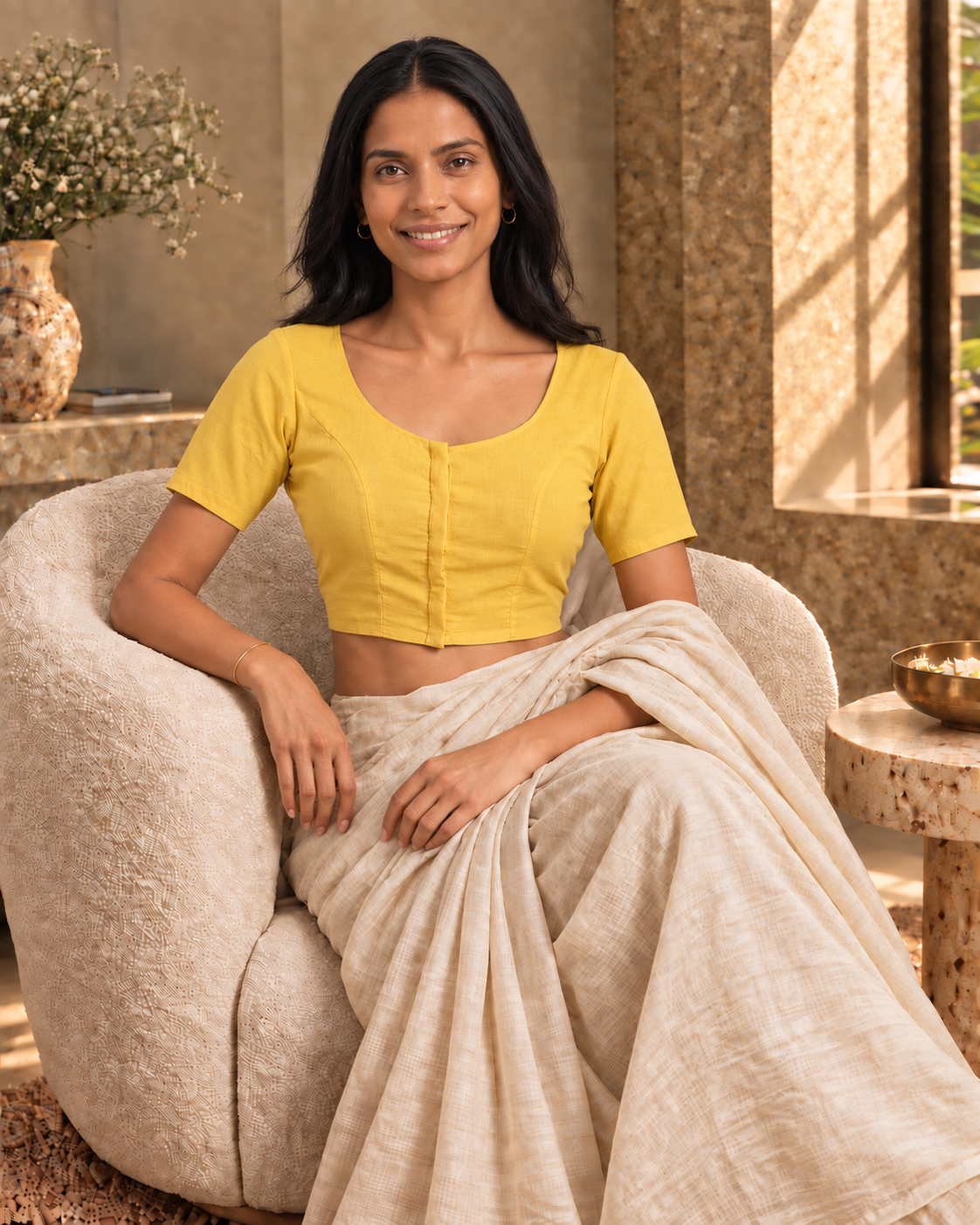 Sunshine yellow front-hook saree blouse worn with a beige saree, seated on a cream boucle armchair